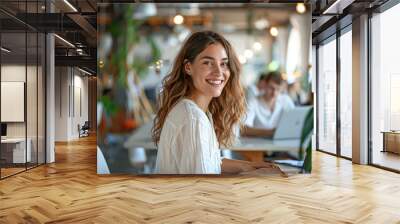 Successful Female Entrepreneur Smiling While Working on Laptop in Bright Startup Office with Team in Background Wall mural