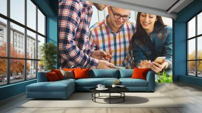 Group of international university students having fun studying in library, three colleagues of modern work co-working space talking and smiling while sitting at the desk table with laptop computer Wall mural