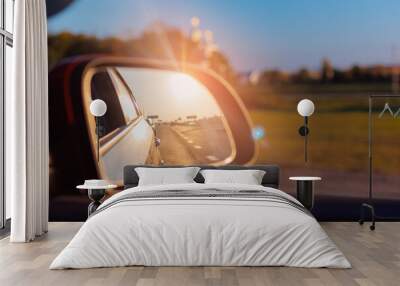 The sun is reflected in the mirror, evening road. View in the side rear view mirror of a red car driving along the highway Wall mural