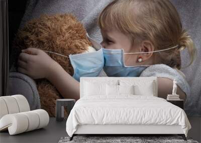 kiss through the medical mask. a small child kisses teddy bear. toy and children in masks. Wall mural