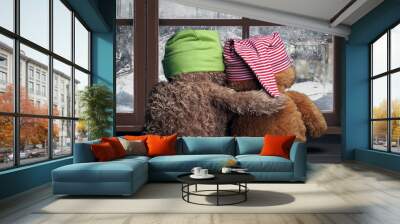 Two friends looking out the window at the falling snow and the city. Toys colorful hats bear cubs. Embrace the . Concept - love, friendship, support Wall mural