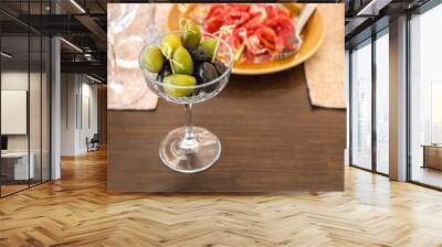 Olives and olives are on the table in a crystal vase on the background of different dishes. Wall mural