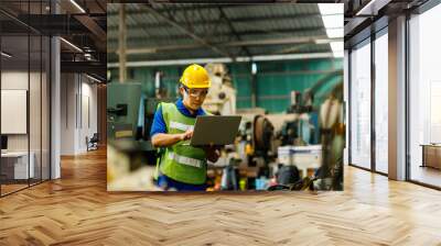 Men industrial engineer in uniform and wearing a Yellow helmet while standing in a heavy industrial factory behind he looking New Project while Using Laptop. Wall mural