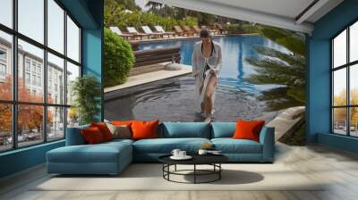 A beautiful hispanic woman leisurely walks by a serene bali resort poolside, embodying tropical elegance. Wall mural