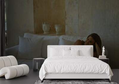 A beautiful hispanic woman relaxing on a white sofa in a typical italian masseria style house indoors. Wall mural