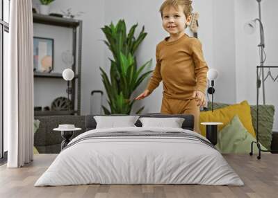 A cheerful blond toddler boy stands on a couch in a modern living room, portraying a playful moment of childhood indoors. Wall mural