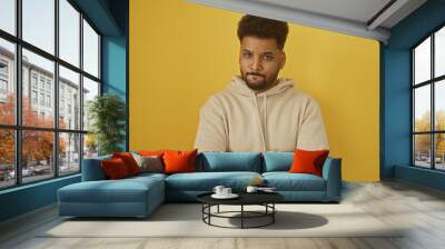 A confident african american man in casual attire posing with folded arms against a yellow background Wall mural