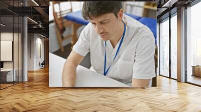 A focused male therapist in a white coat working in a bright physiotherapy clinic. Wall mural