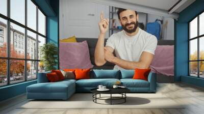 a happy bearded man in casual attire gesturing an idea while sitting on a couch indoors. Wall mural