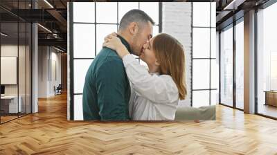 A loving couple embracing and kissing in a bright, modern living room with large windows. Wall mural