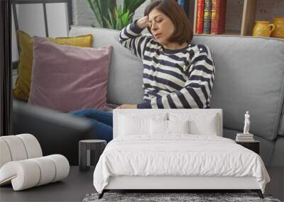 A mature hispanic woman in casual attire relaxes on a sofa in a cozy living room, embodying a moment of tranquility. Wall mural