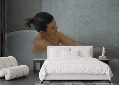 A serene woman relaxes in a bubble bath at a luxurious marble bathroom, exuding tranquility and self-care. Wall mural