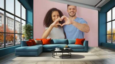 A smiling man and woman make a heart shape with their hands against a pink background, depicting affection and unity. Wall mural