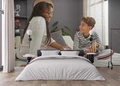 A smiling woman and boy sitting together on a bed, sharing a moment in a cozy bedroom setting Wall mural