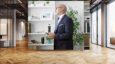 A sophisticated mature man in a suit gazes at something in a modern office. Wall mural