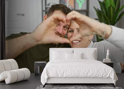 A woman and a man form a heart shape with their hands, showcasing affection in a light indoor setting. Wall mural