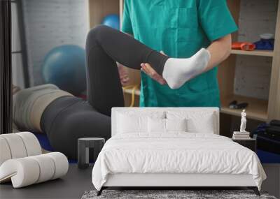 A woman patient undergoes leg rehabilitation with a male physiotherapist in an indoor clinic setting Wall mural