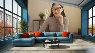 A young asian woman wearing glasses in a modern home interior, seated at a desk with a laptop, portrays professionalism and style. Wall mural