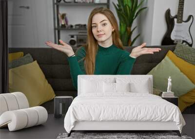 A young blonde woman sits casually on a gray couch in a modern living room, gesturing with open hands. Wall mural