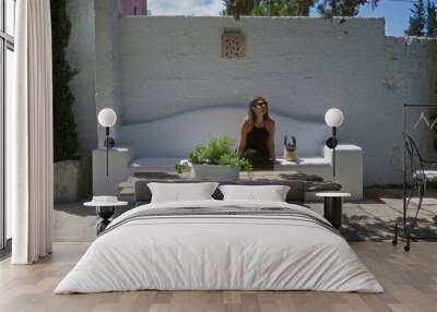 A young hispanic woman sits in a beautiful, sunny outdoor space at an italian villa in puglia, europe, enjoying the serene atmosphere of her home garden. Wall mural