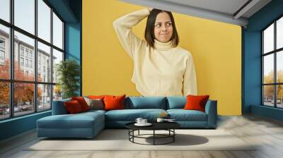 A young hispanic woman with a casual hairstyle poses confidently against an isolated yellow background, exuding beauty and charm. Wall mural