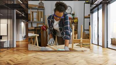 A young woman sands wood in a well-equipped indoor carpentry workshop. Wall mural