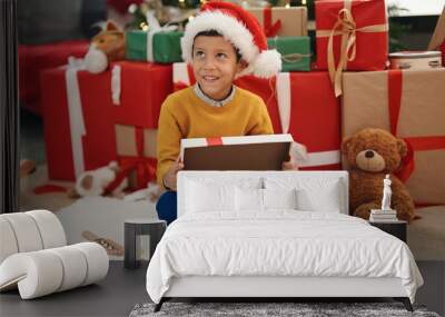 Adorable hispanic boy unpacking gift sitting by christmas tree at home Wall mural