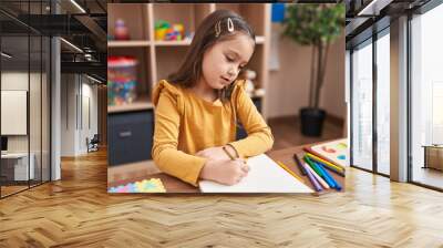 Adorable hispanic girl student sitting on table drawing on paper at kindergarten Wall mural