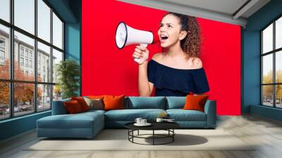 Adorable latin teenager girl with angry expression. Screaming loud using megaphone standing over isolated red background Wall mural