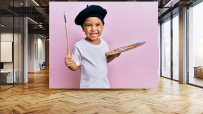 Adorable latin toddler smiling happy wearing artist style using paintbrush and palette over isolated pink background. Wall mural