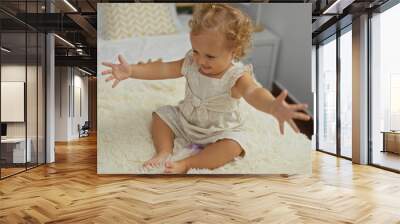 Adorable toddler girl with blonde hair enjoying childhood while sitting on a bed in a cozy indoor home bedroom Wall mural