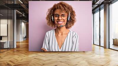 African american curly call center agent woman working using headset over pink background happy face smiling with crossed arms looking at the camera. Positive person. Wall mural