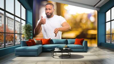 African american man with beard confused with thumbs up and down, trying to take a decision expressing doubt and frustration at night Wall mural