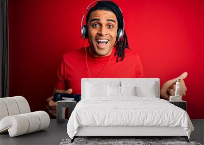 African american man with dreadlocks playing video game using joystick and headphones screaming proud and celebrating victory and success very excited, cheering emotion Wall mural