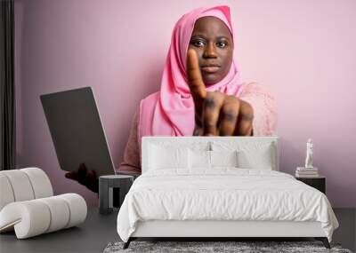 African american plus size woman wearing muslim hijab using laptop over pink background Pointing with finger up and angry expression, showing no gesture Wall mural