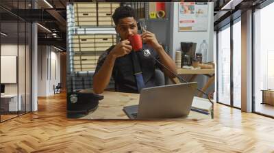 African american police officer sipping coffee while on a phone call in a cluttered office setting Wall mural