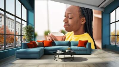 African american woman drinking coffee sitting on table at home Wall mural