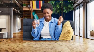 African american woman drinking glass of water screaming proud, celebrating victory and success very excited with raised arm Wall mural