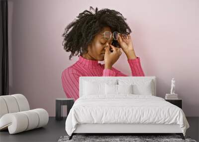 African american woman in pink touching her nose indoors, portraying tiredness or allergy symptoms. Wall mural