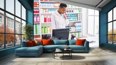 African american woman pharmacist talking on telephone using computer at pharmacy Wall mural