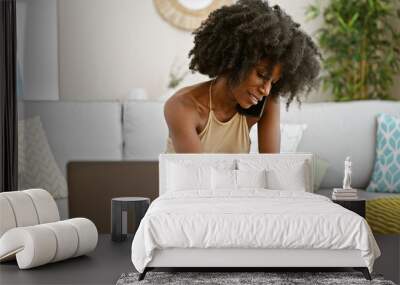 African american woman talking on smartphone using laptop taking notes at home Wall mural