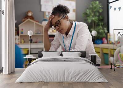 African american woman teacher overworked collecting toys at kindergarten Wall mural