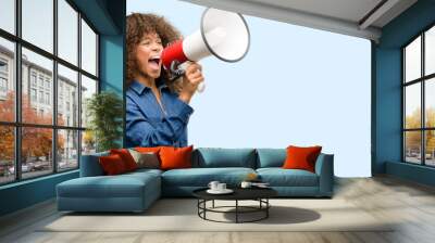 african american woman wearing blue jumpsuit communicates shouting loud holding a megaphone, express Wall mural