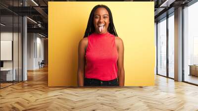 African american woman wearing red casual t-shirt standing over isolated yellow background sticking tongue out happy with funny expression. Emotion concept. Wall mural