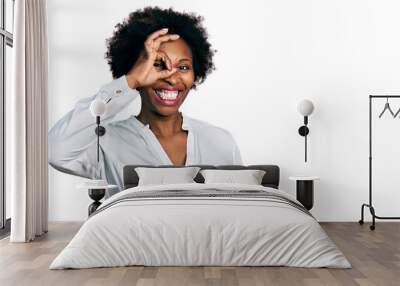 African american woman with afro hair wearing casual white t shirt doing ok gesture with hand smiling, eye looking through fingers with happy face. Wall mural