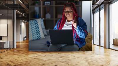 African american woman with braided hair using computer laptop at night pointing up looking sad and upset, indicating direction with fingers, unhappy and depressed. Wall mural