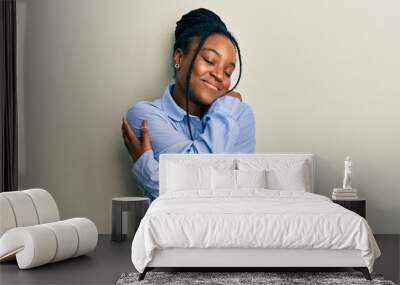 African american woman with braided hair wearing casual blue shirt hugging oneself happy and positive, smiling confident. self love and self care Wall mural