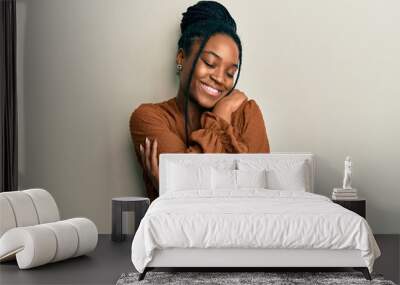 African american woman with braided hair wearing casual brown shirt hugging oneself happy and positive, smiling confident. self love and self care Wall mural