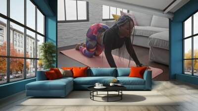 African american woman with braids practicing yoga in a stylish living room setting. Wall mural