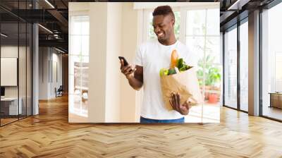 African man holding a paper bag full of groceries and using smarpthone buying online using app smiling Wall mural